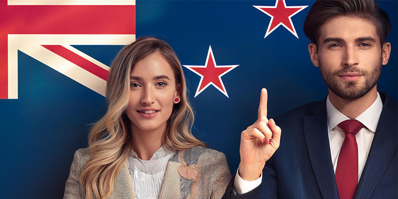 Two professional individuals standing in front of the New Zealand flag, representing New Zealand culture. The image aligns with an article discussing Kiwi slang, showcasing national pride and identity.